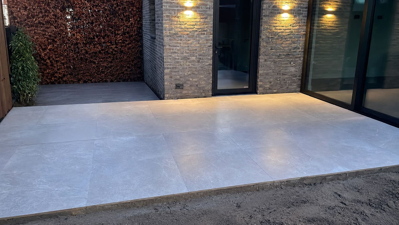 Nieuw aangelegd terras van grote lichtgrijze keramische tegels bij openslaande deuren